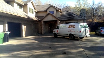 ACDC van in a brick-house driveway with hoses running to the job