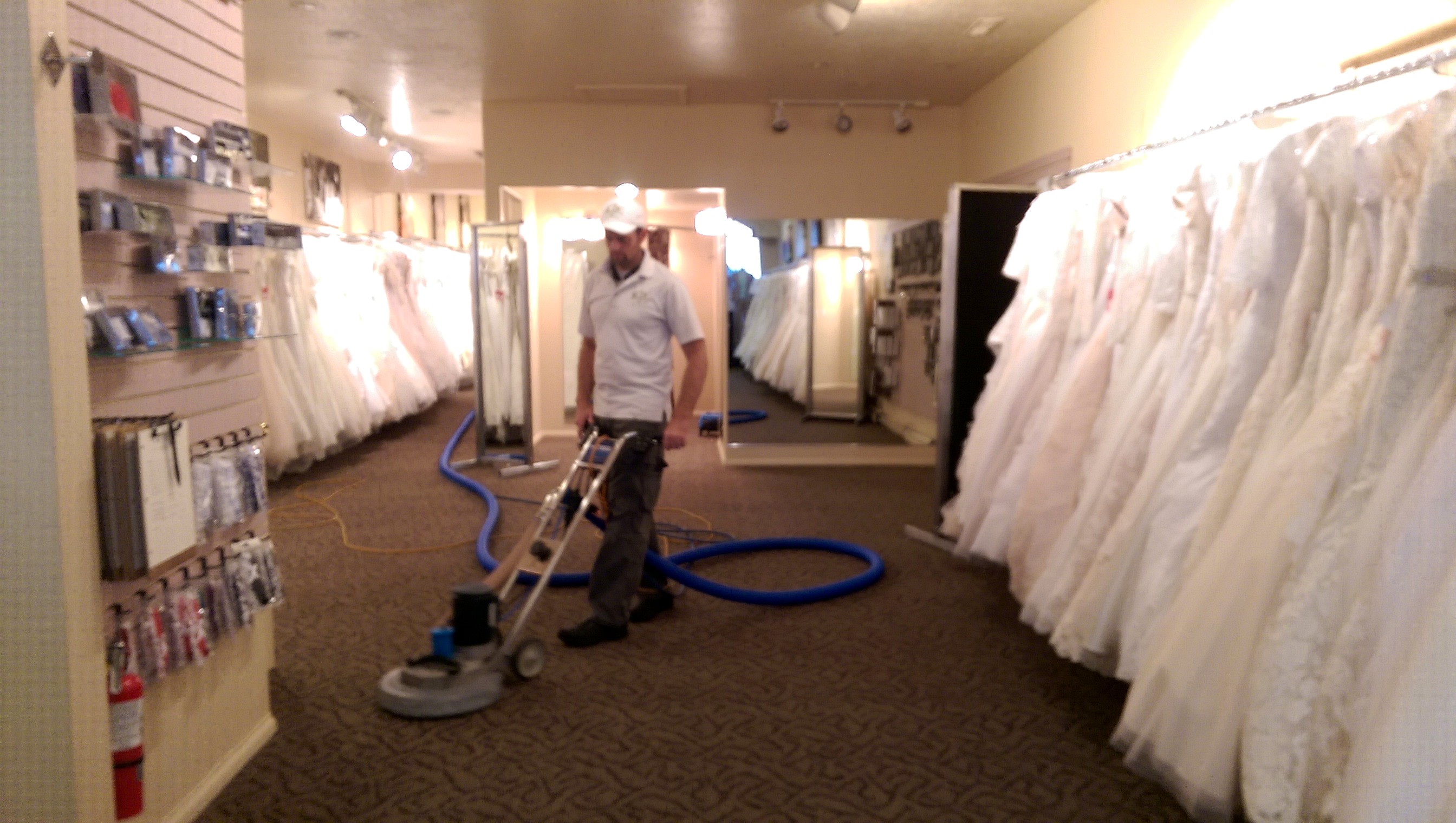 Technician extracting carpet in a bridal shop with wedding dresses on the racks
